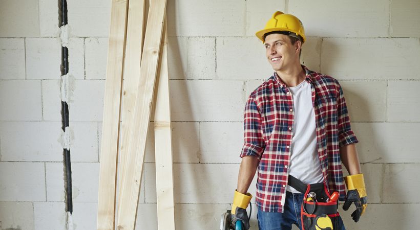 Young carpenter is holding electric saw and looking away